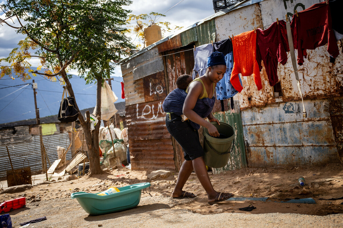 Primrose, en ung kvinna, har sitt barn på ryggen och hänger tvätt, Sydafrika.